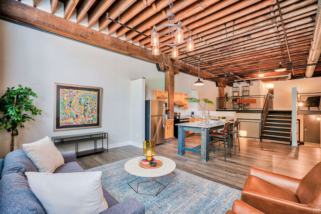 A living room with wooden ceiling panels near a kitchen with a small staircase leading to a lofted area at Wireworks Lofts in the Square.