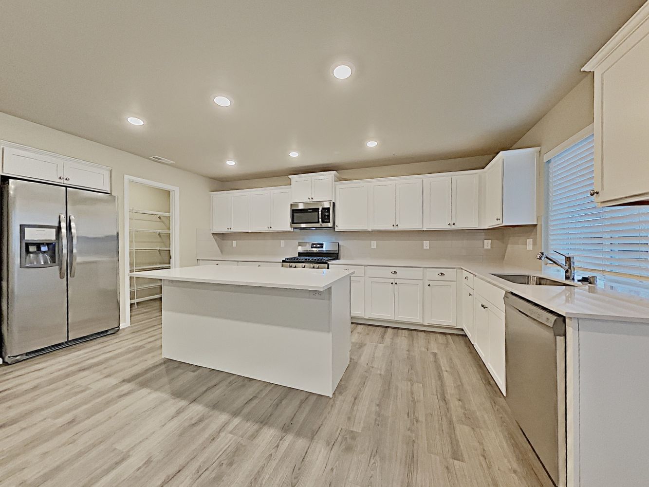 Kitchen with luxury vinyl plank flooring, quartz countertops, stainless-steel appliances, a large island and spacious pantry at Invitation Homes Seattle.