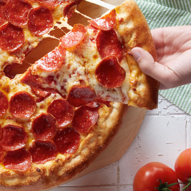 Une personne retirant une part d'une pizza pepperoni de Romeo's.