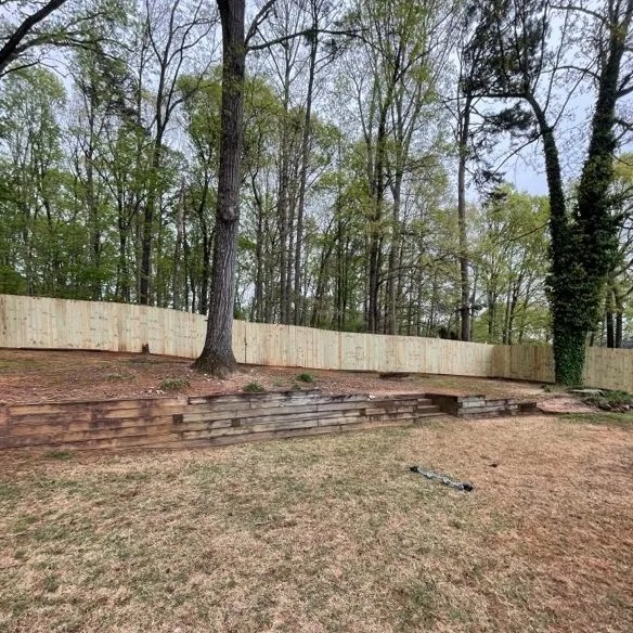 Backyard with wooden retaining wall, tall trees, and newly installed fence.