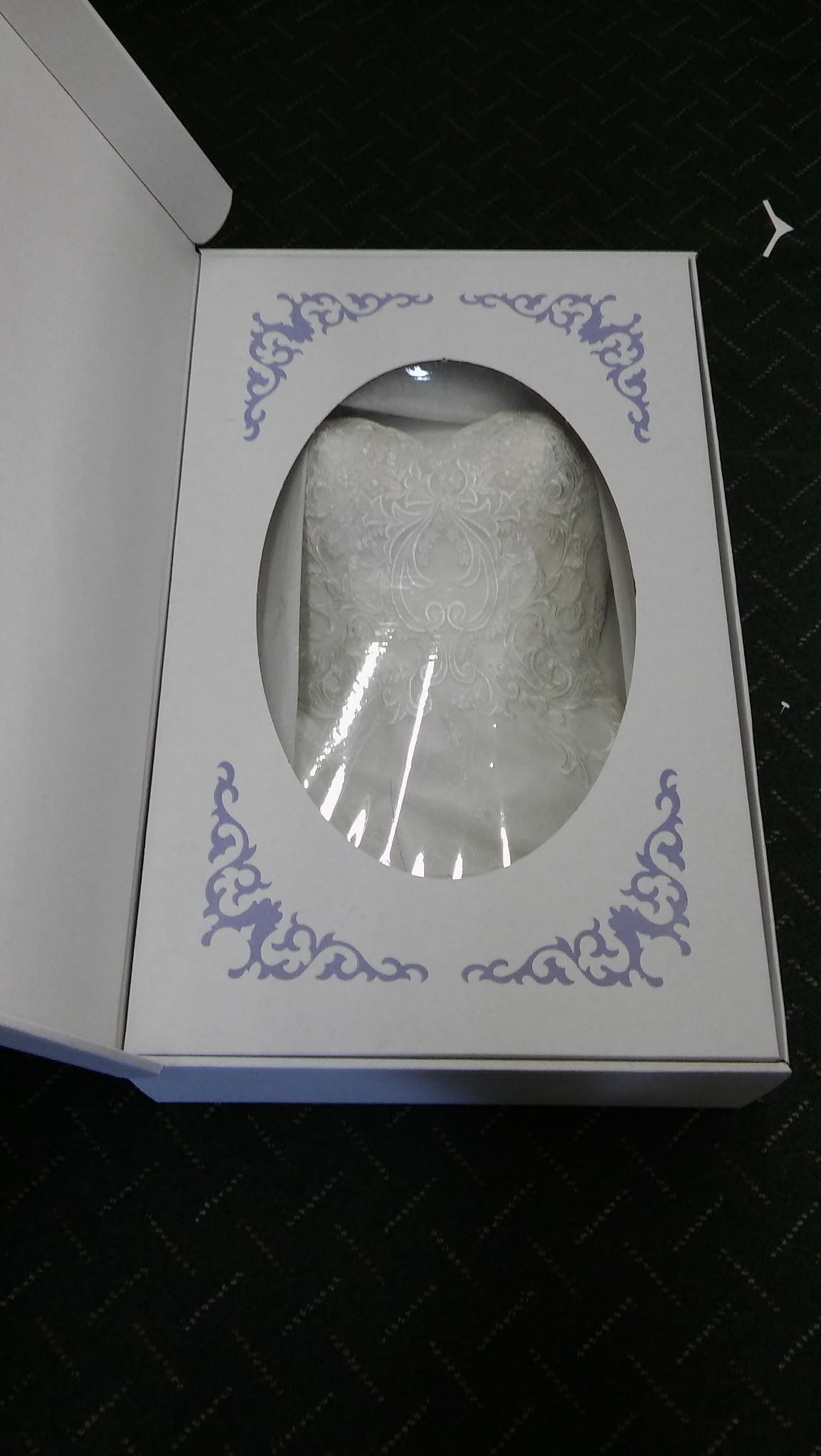 A preserved wedding dress safely sealed inside a white decorative archival storage box with a viewing window at Plaza Cleaners