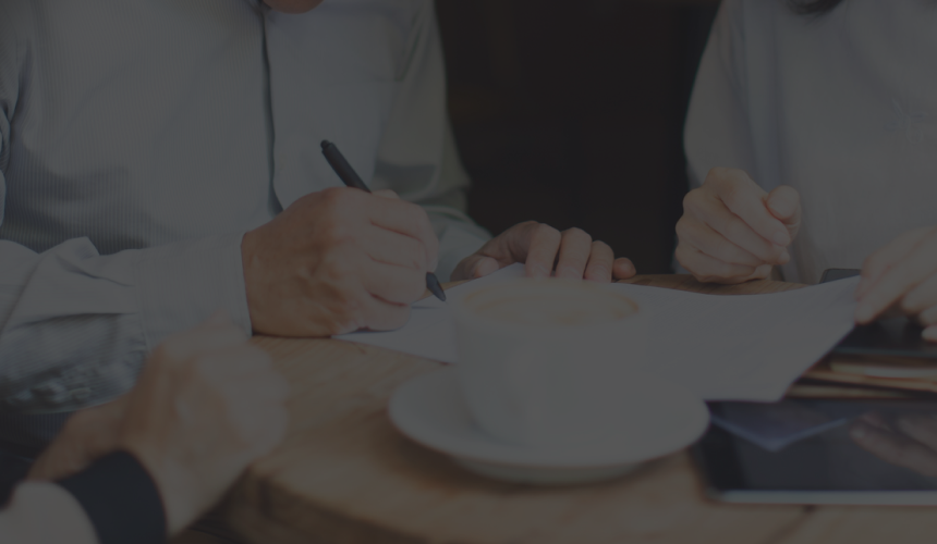 Close-up shot of people gathered around a cafe table signing a document.