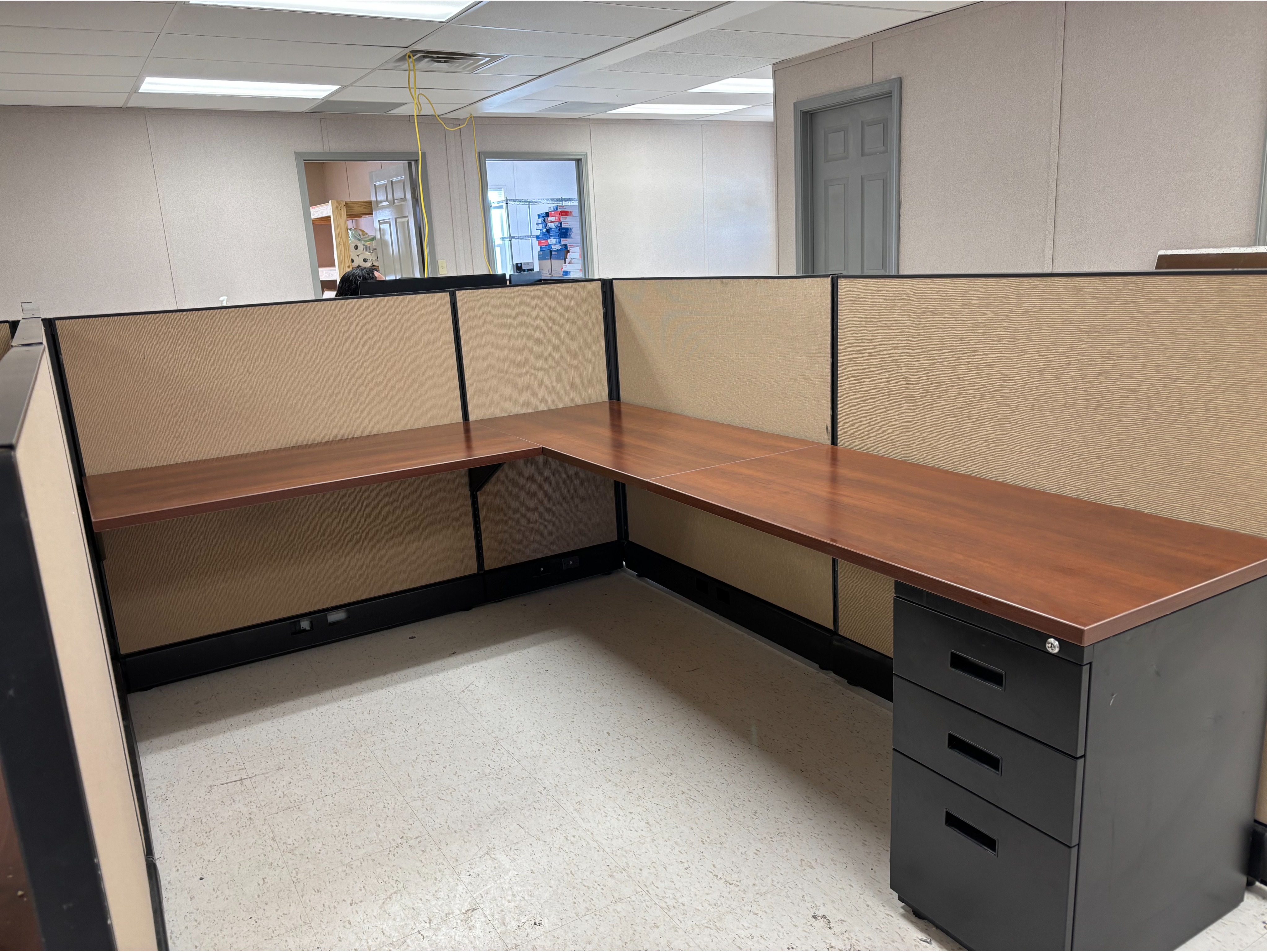 Large Corner Office Pod:

Spacious multi-person corner cubicle setup with dark trim, warm wood-laminate desks, integrated storage pedestals, and neutral fabric divider walls.