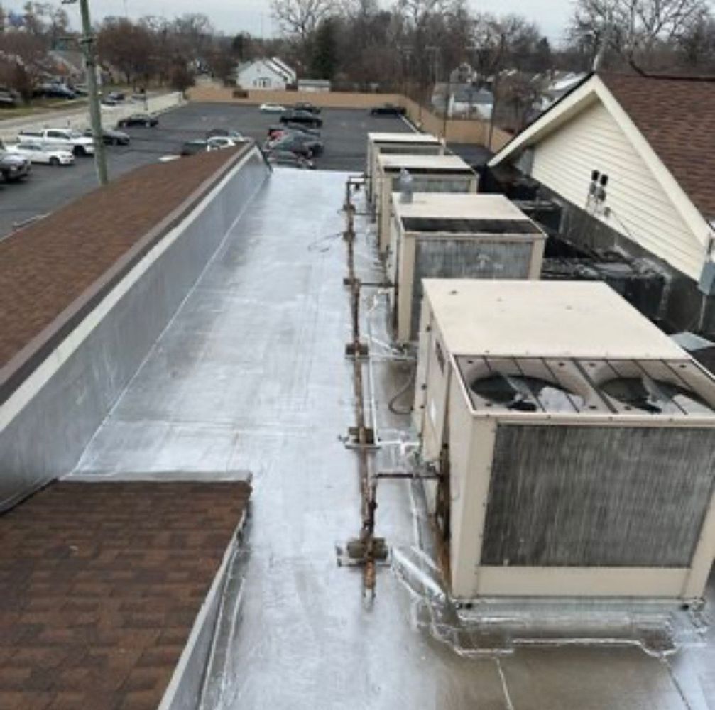 View of a completed flat roof installation featuring a reflective or metallic surface. A neat row of large HVAC units is prominent, with associated piping visible. Adjacent roof sections are nearby.