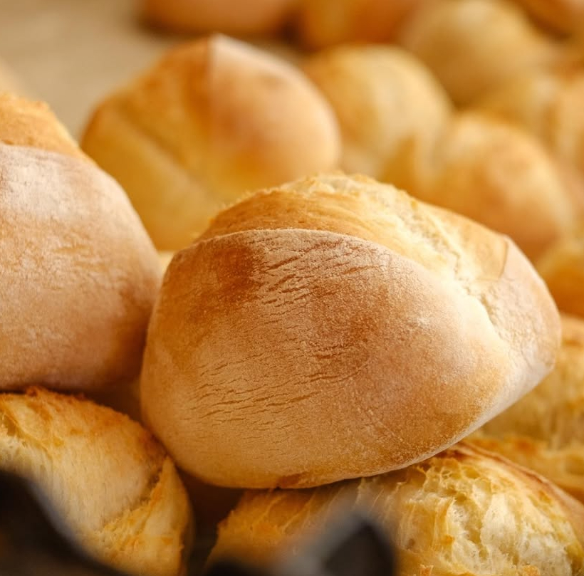 A close-up view of crusty, golden-brown artisan bread rolls displayed at a local bakery vendor booth. The focus highlights the dusted flour and crispy textures of fresh-baked goods.