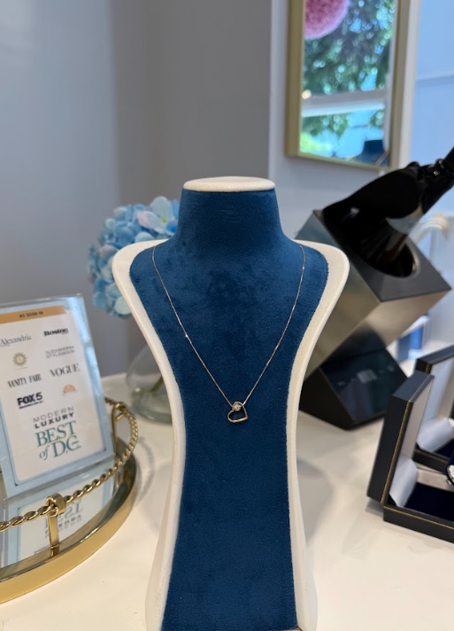 A delicate designer pendant necklace is elegantly displayed on a blue velvet jewelry stand at Eliana Curated, accompanied by its Modern Luxury Best of DC recognition and other fine jewelry pieces.