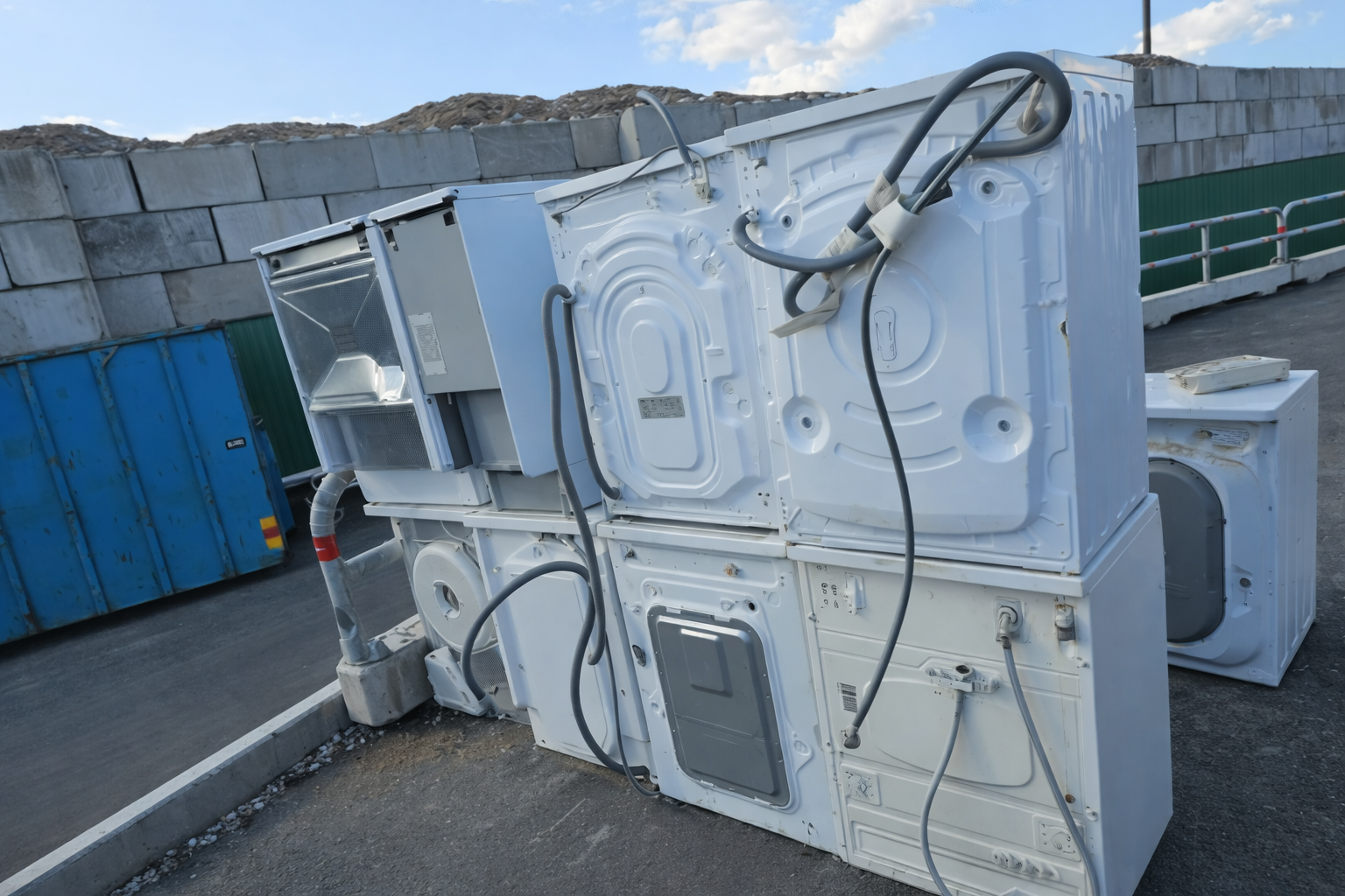 Discarded household appliances stacked outdoors, including washing machines and dryers, representing bulk junk removal, appliance disposal services, and recycling or waste management operations.