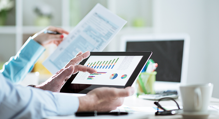 Two people looking at charts on a tablet and information in a printed document.