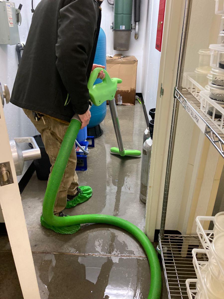 Water Tech in beige pants and black jacket with green water extractor.