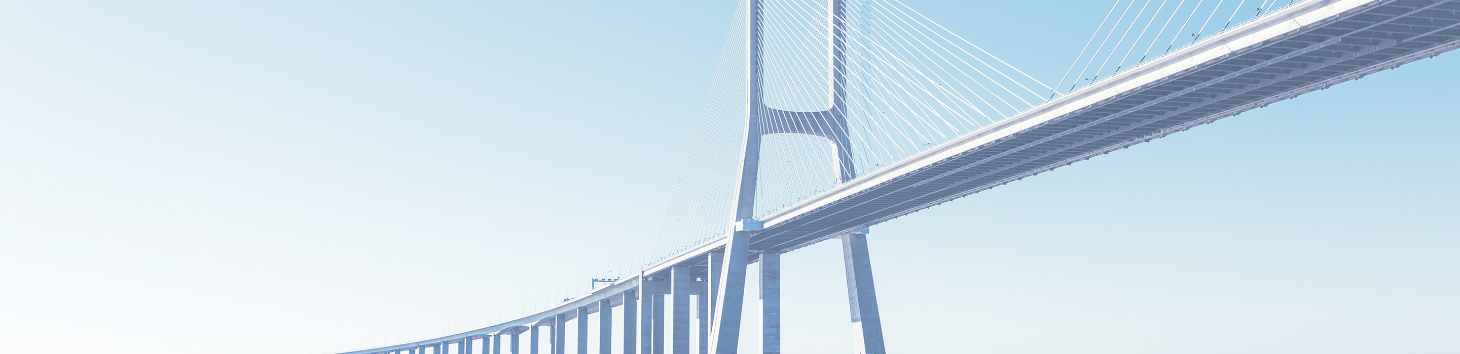 Long cable-stayed suspension bridge spanning across calm blue water under clear sky.
