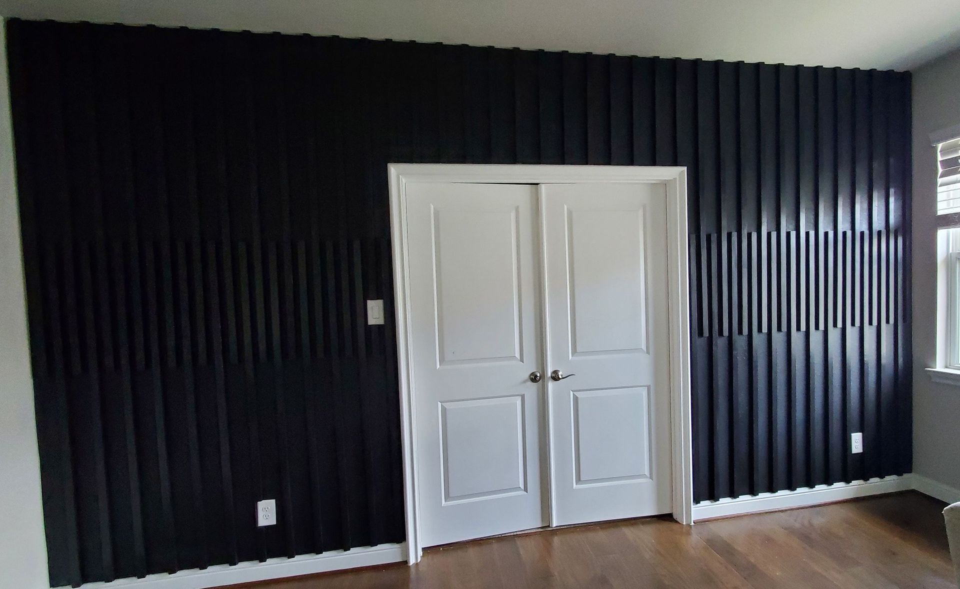 Modern room featuring a dramatic black slatted accent wall surrounding double doors, adding texture, depth, and contemporary elegance while complementing hardwood flooring and minimalist interior finishes beautifully.