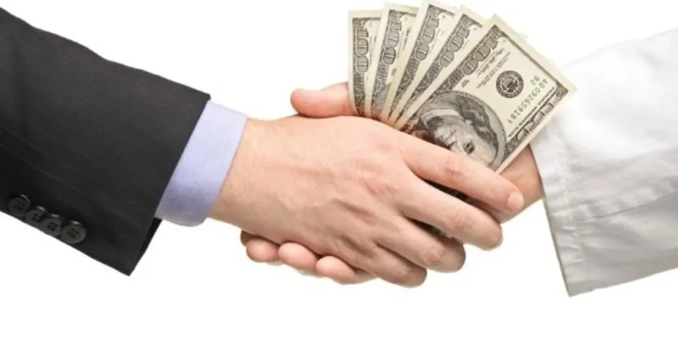 Two hands are shaking, with one hand holding a fan of US one-hundred dollar bills, suggesting a transaction or deal involving money.