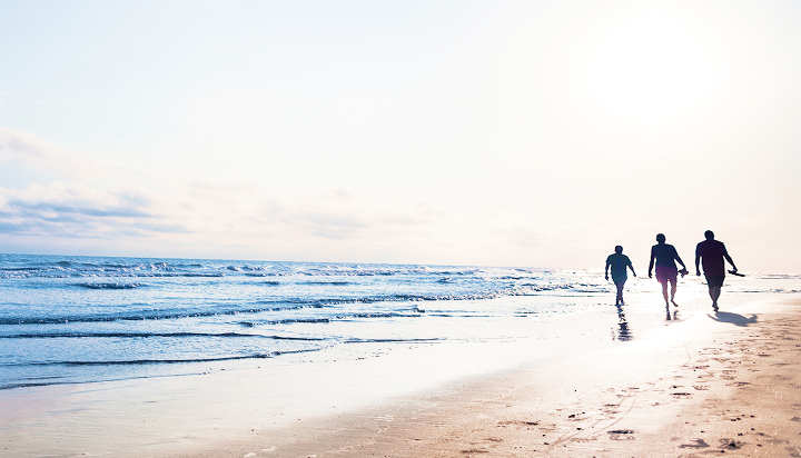 Three people walking on a beach.