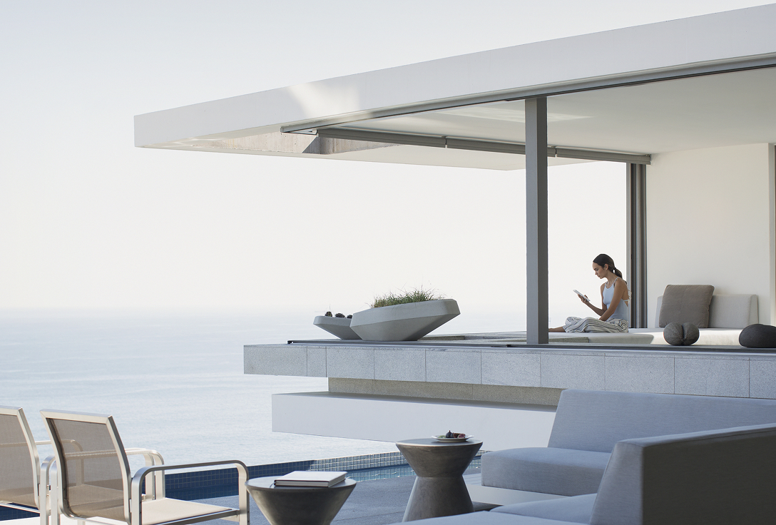 Modern seaside patio with minimalist furniture overlooking the ocean. A person relaxes, reading and conveying a calm, peaceful atmosphere.