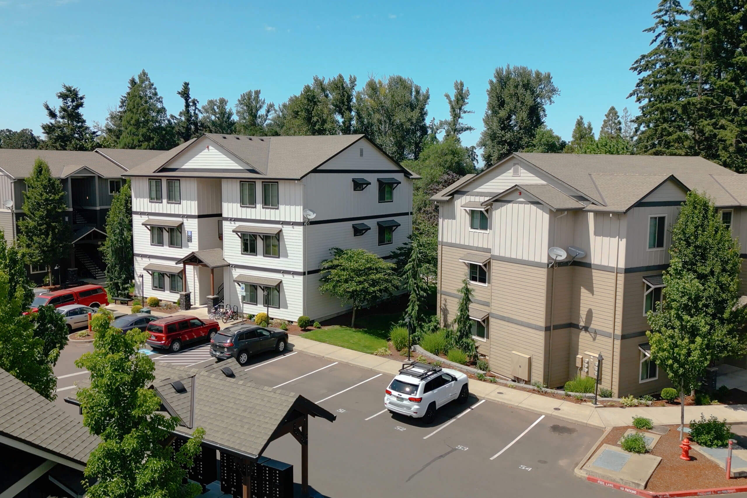 A white and beige apartment complex with a parking lot in front.