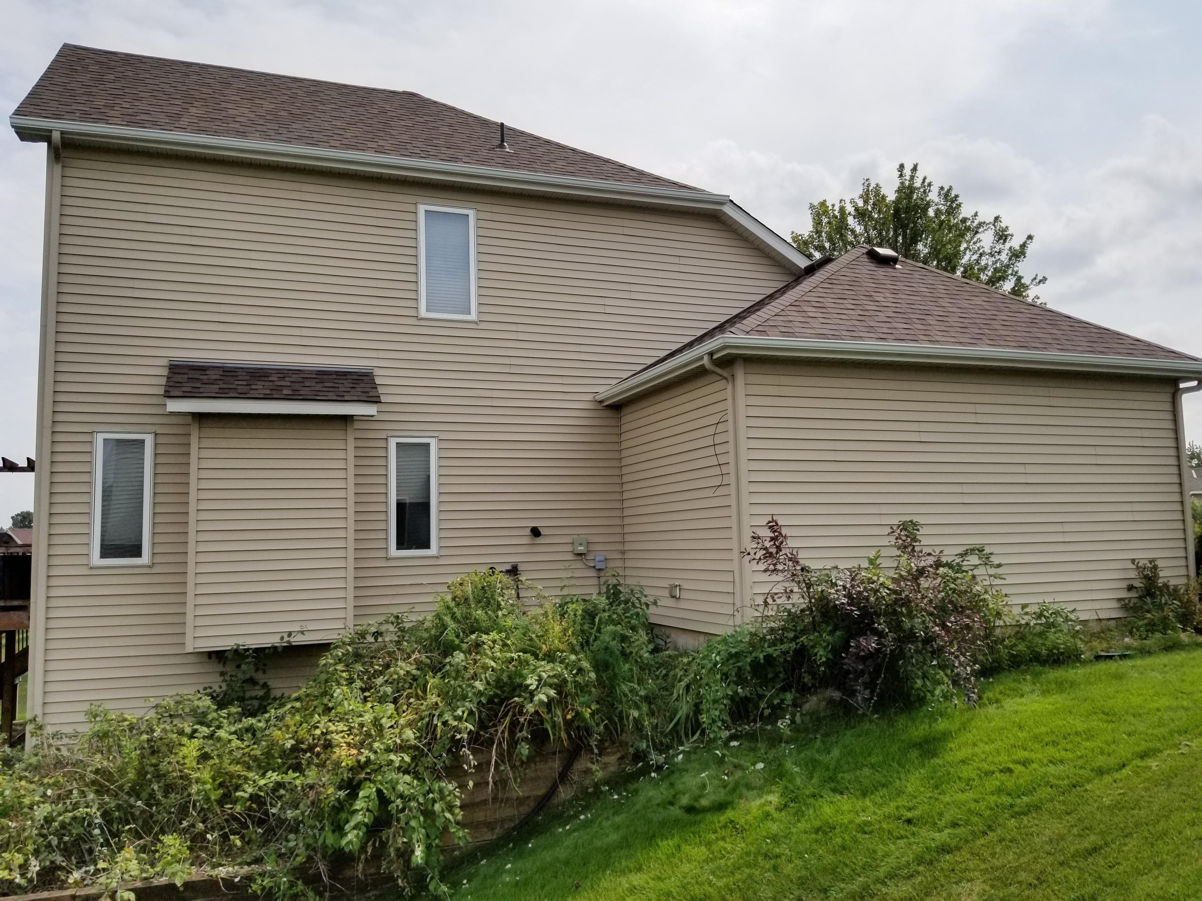 White seamless gutters and downspouts installed on the side and rear of a two-story tan home by Ultimate Gutter Solutions.