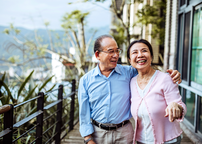 A couple smiling on a balcony with a scenic view.