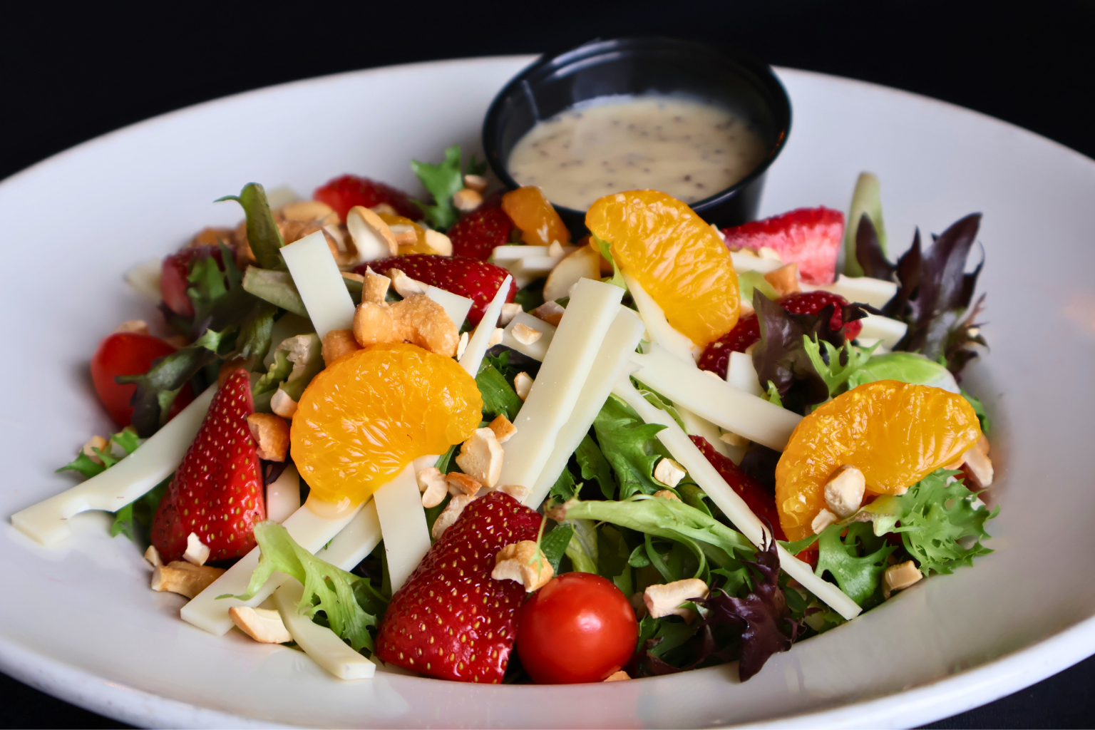 Uccello’s Riviera Salad with garden greens, strawberries, mandarin oranges, tomatoes, Swiss cheese, and cashews on a white plate, served with a breadstick and poppy seed dressing inside Uccello’s Ristorante.