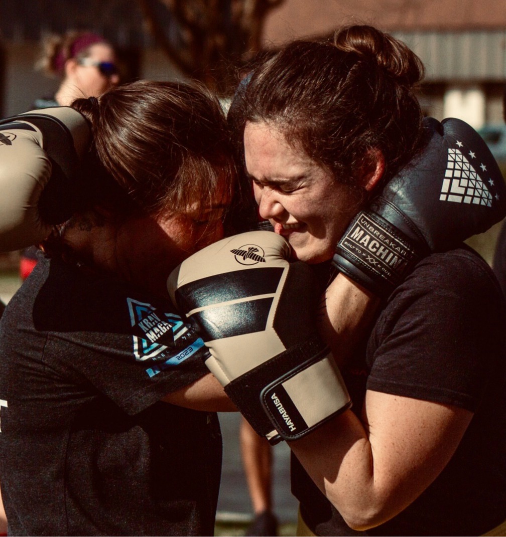 Two adult students in a close-range clinch during outdoor sparring rounds.
