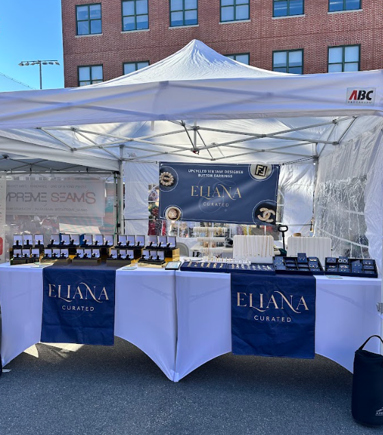 Eliana Curated showcases upcycled vintage designer jewelry and luxury accessories at an elegant outdoor pop-up booth, featuring beautifully arranged necklaces, bracelets, earrings, and rings.
