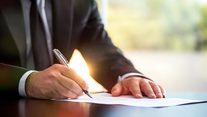 A person signing a document at a desk.