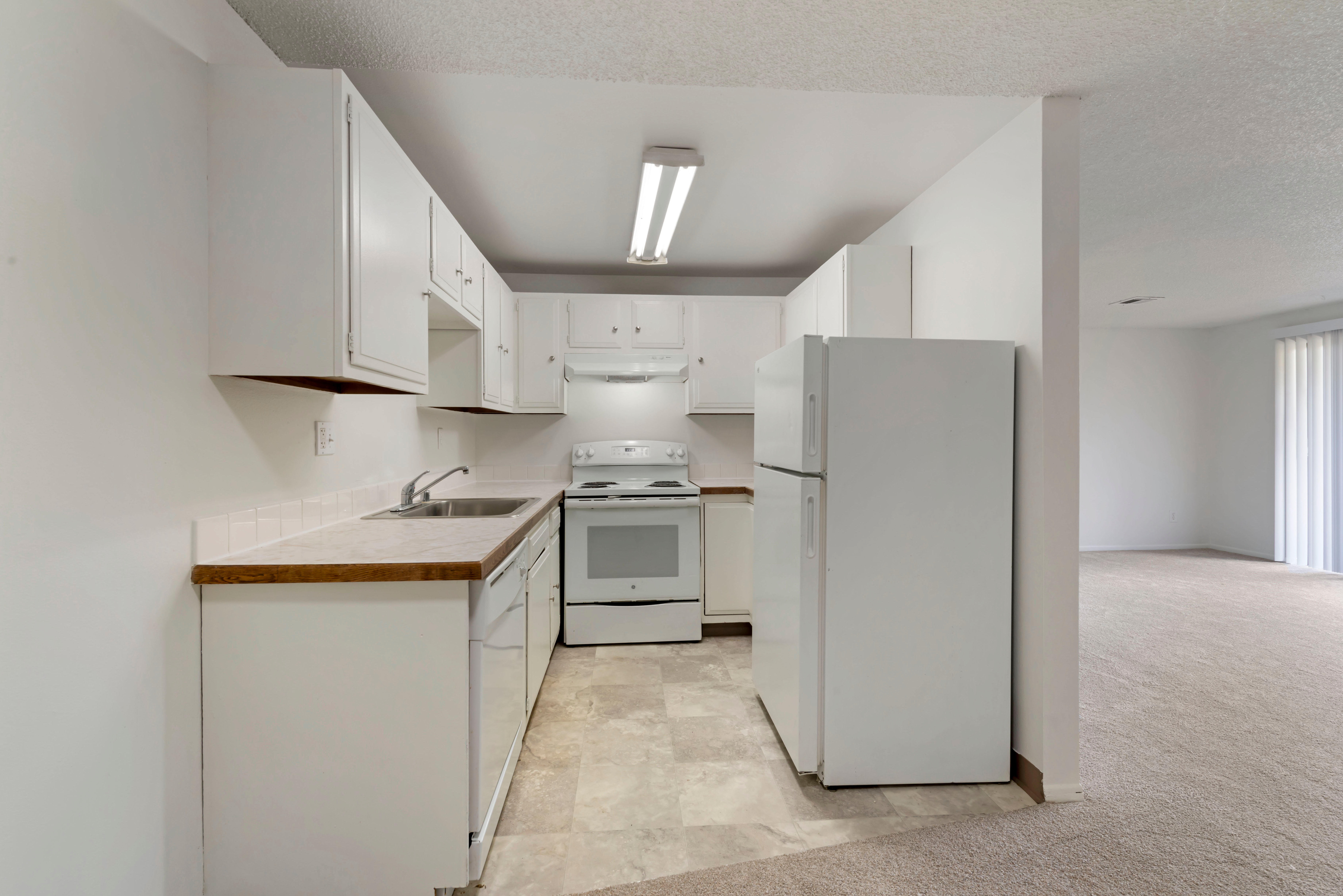 Tile-floored kitchen with white appliances, white cabinets, and laminate counters.