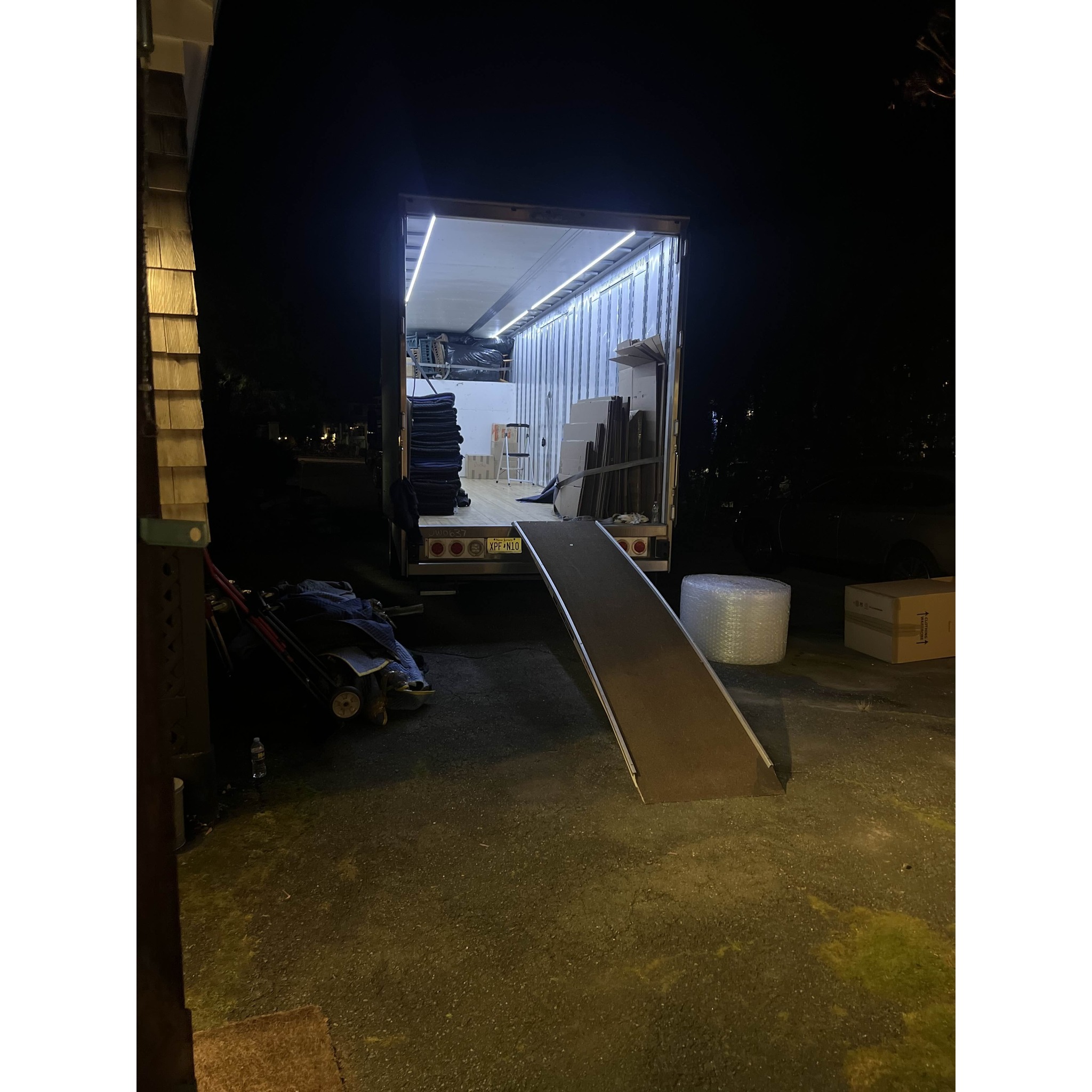 Night move setup with an M&M Movers truck open and lit, ramp in place, and moving blankets and packing materials staged for secure loading and transport.