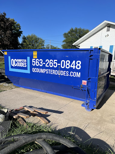 A blue QC Dumpster Dudes dumpster placed in a residential driveway, ready for household cleanup or renovation debris.