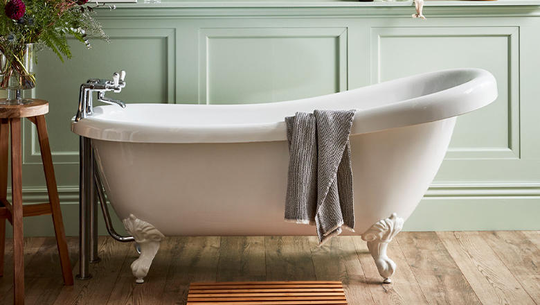 A white roll top bath on silver legs with silver taps stands in a green wall panelled bathroom