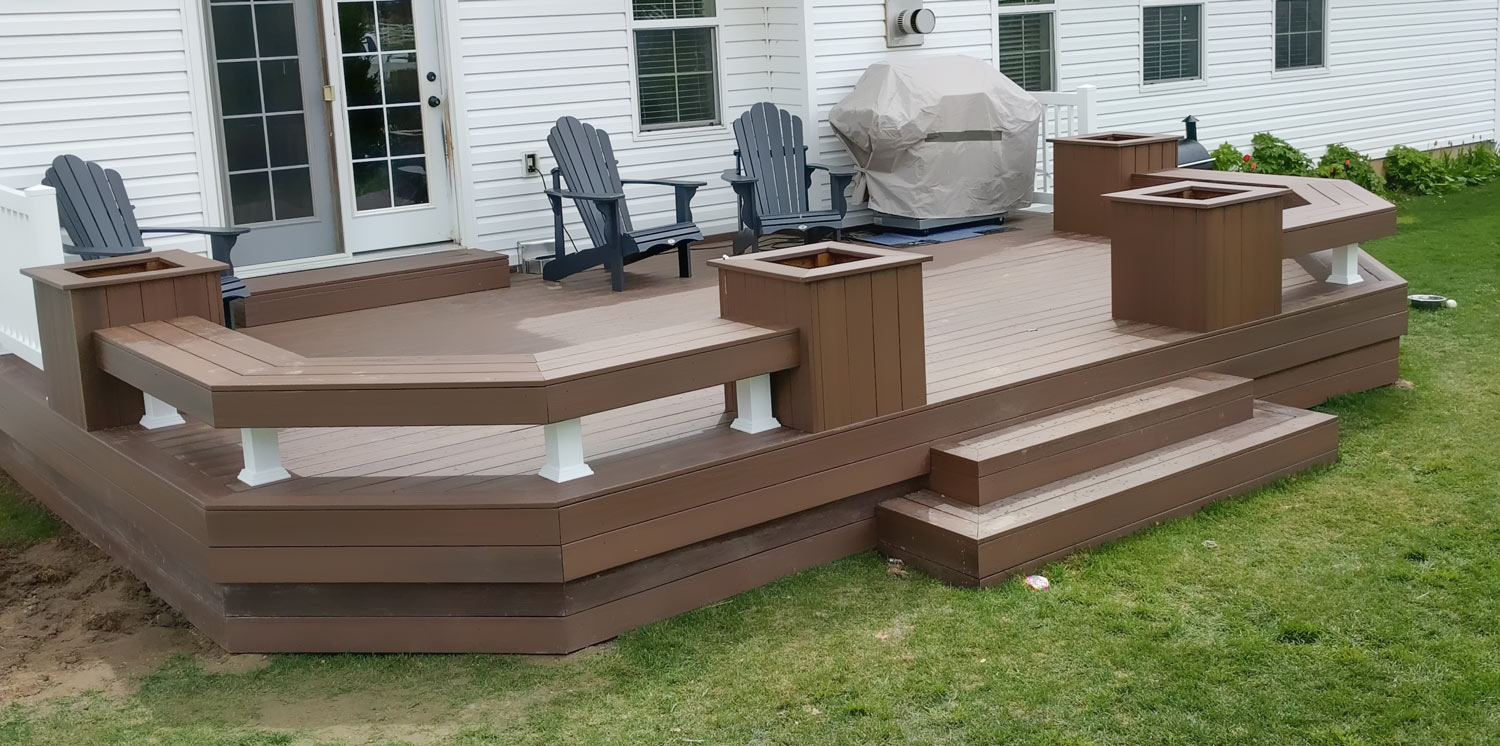 Maximize your backyard entertainment space with this custom ground-level composite deck by DeckPro LLC. Designed for both style and function, it features extensive built-in benches with integrated planter boxes, providing ample seating without cluttering the space. The durable brown composite material ensures a beautiful, low-maintenance finish for years to come.