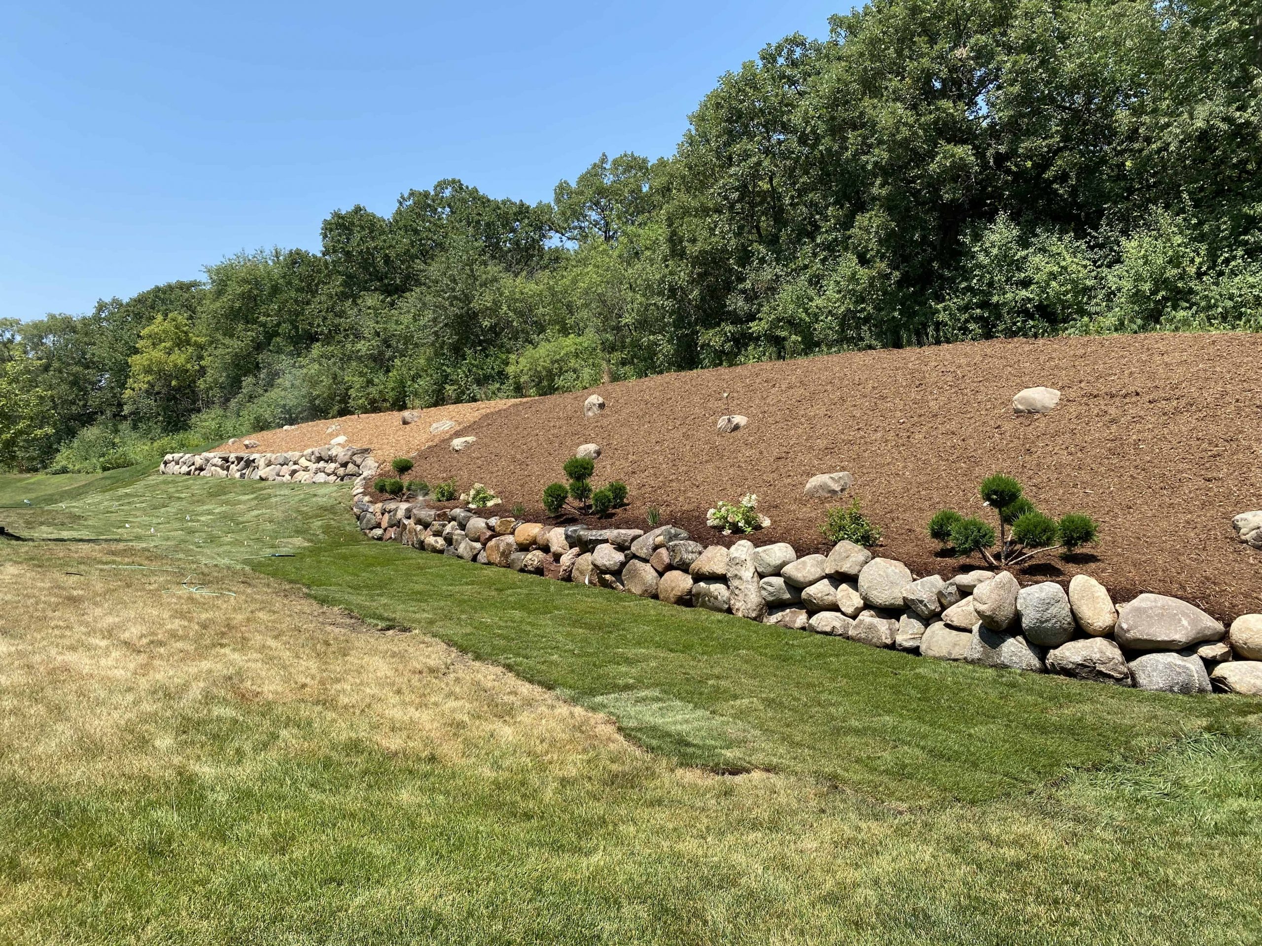Natural boulders, fresh mulch, and new plantings come together for a hillside that's both beautiful and protected from erosion.