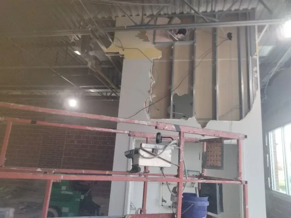 Interior demolition work in commercial building showing partially removed wall, exposed framing, wir 