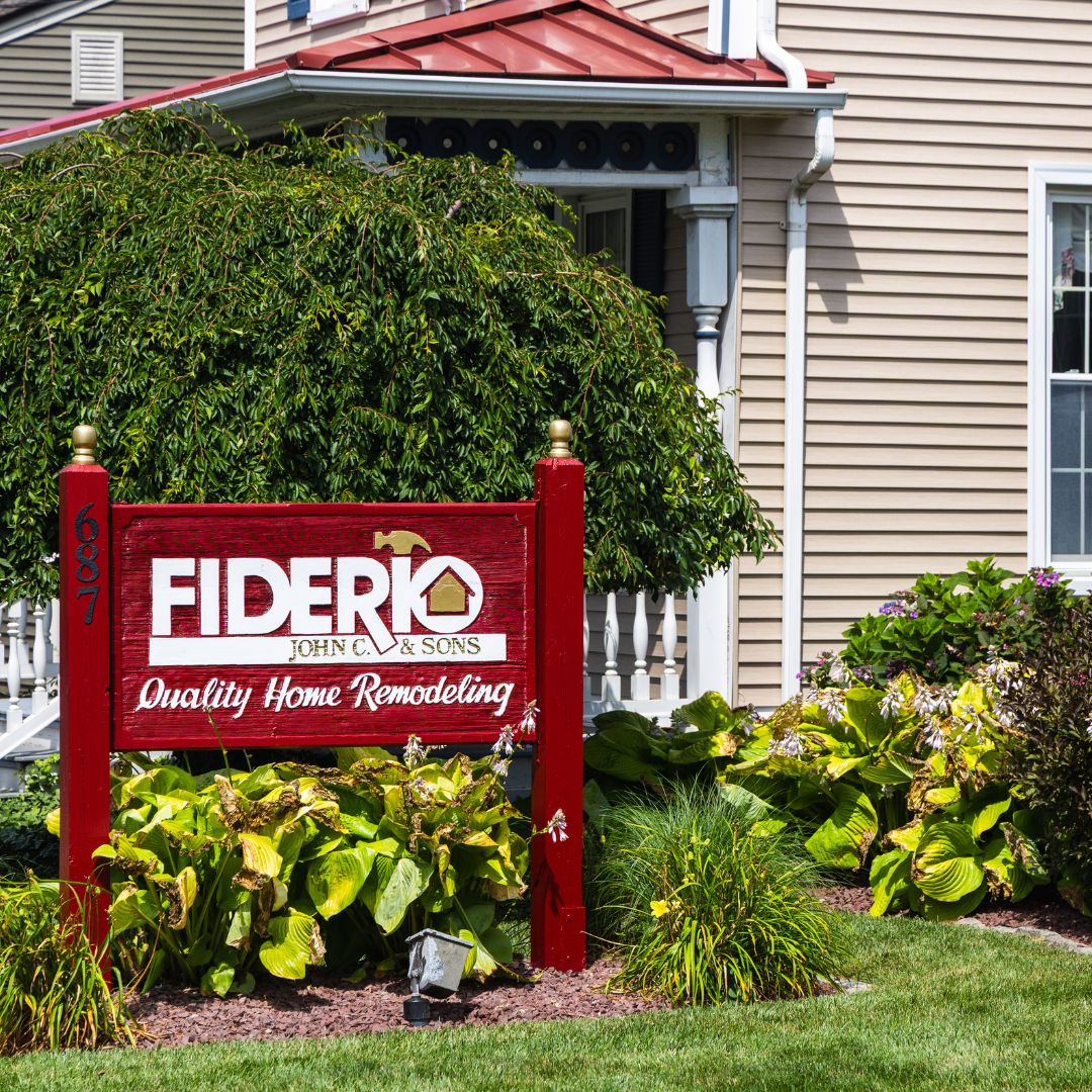 Detailed shot of the red Fiderio & Sons sign in front of the office, surrounded by vibrant hostas and flowering shrubs.
