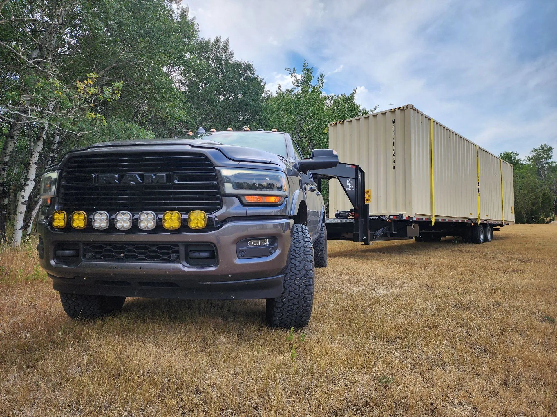 Heavy-duty pickup truck towing a large portable storage container on trailer across grassy field, demonstrating reliable transportation, delivery capability, and mobility of storage units for residential and commercial use.