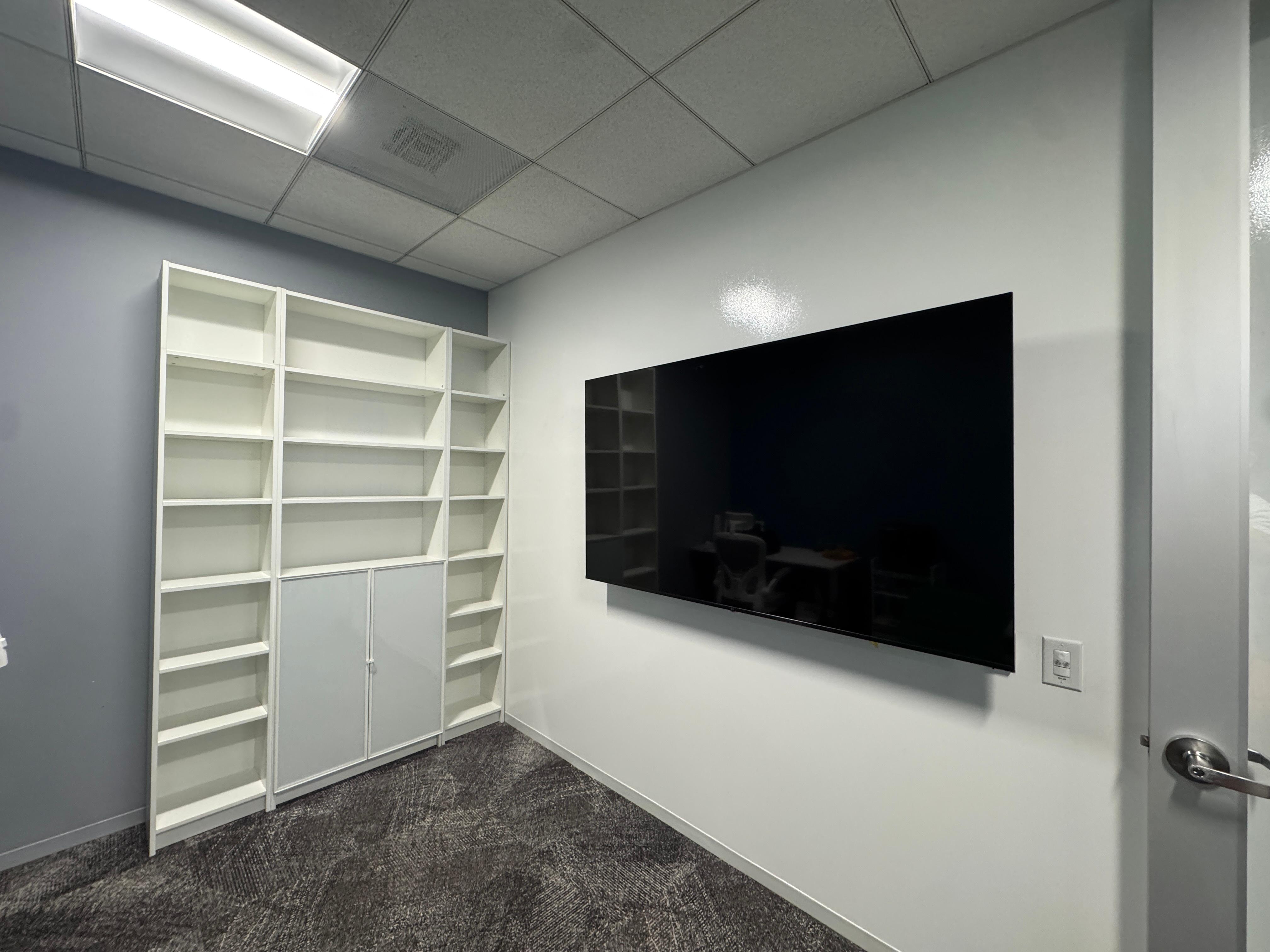 75-inch Samsung TV mounted on a wall beside assembled IKEA BILLY and H&Ouml;GBO shelving in a commercial office.