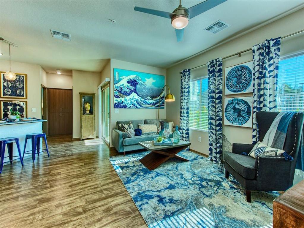 A living area of an apartment with wood floors with a blue patterned rug and a ceiling fan
