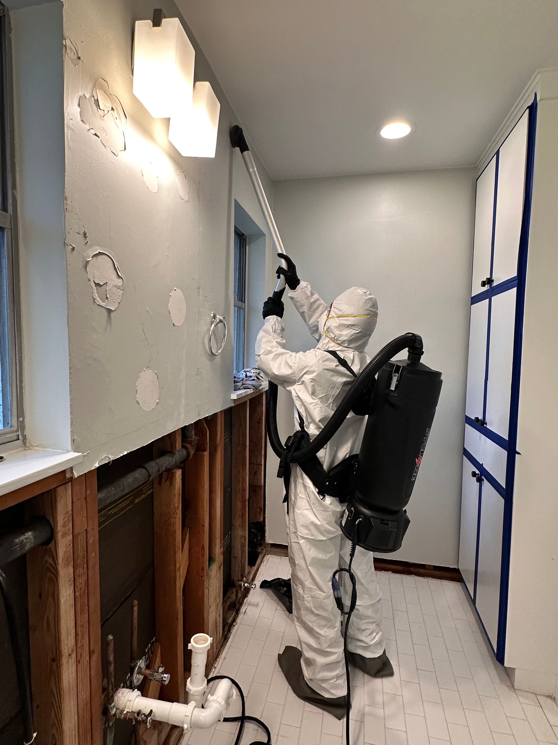 A restoration technician wearing protective coveralls uses specialized cleaning equipment on a damag 