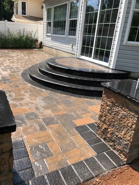 A newly paved backyard patio with a curved set of steps leading up to a sliding glass door, adjacent to a house.