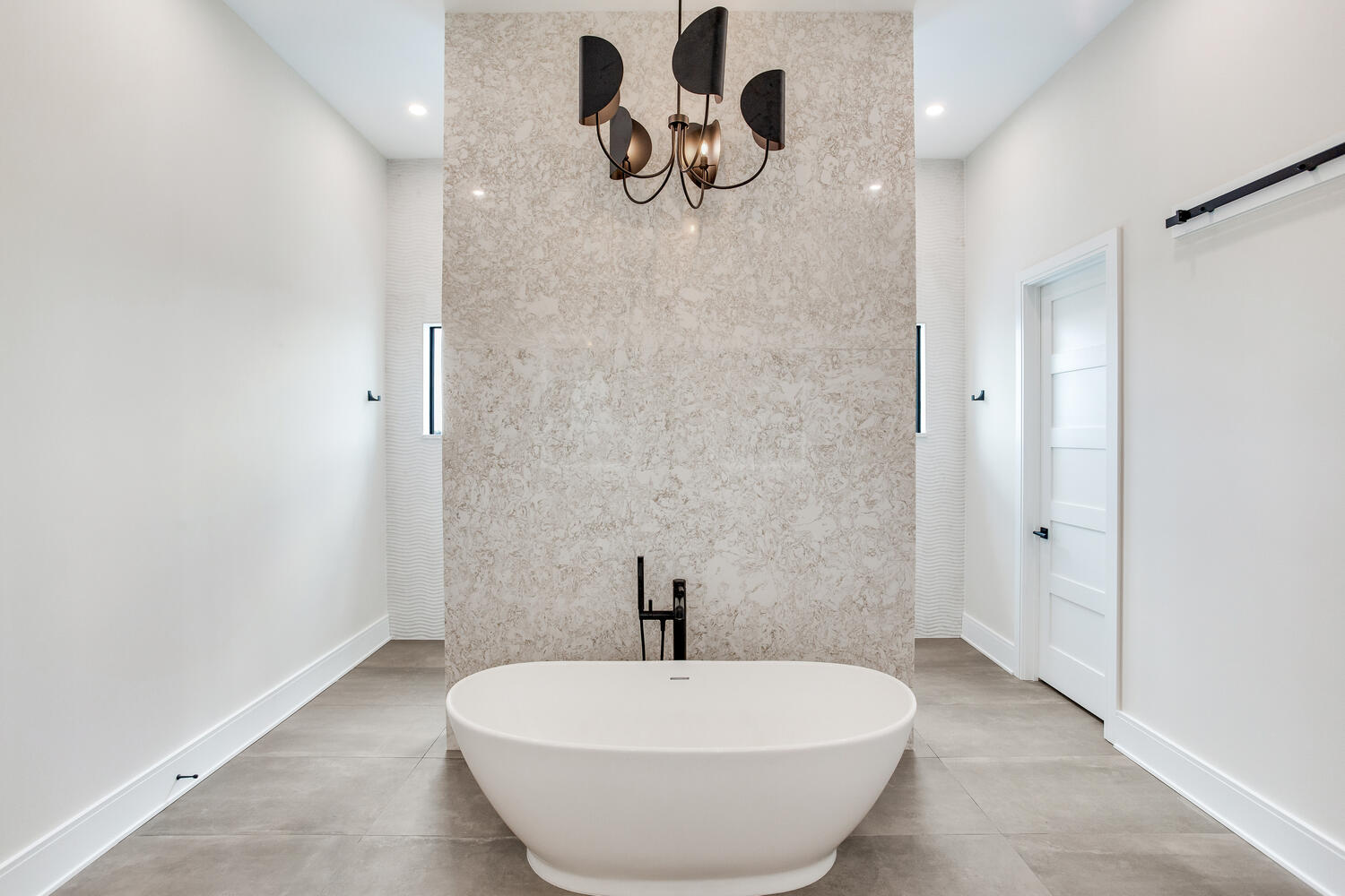 Spa-inspired bathroom with a freestanding soaking tub, walk-in shower, marble-look tile, modern chandelier, and clean luxury design.