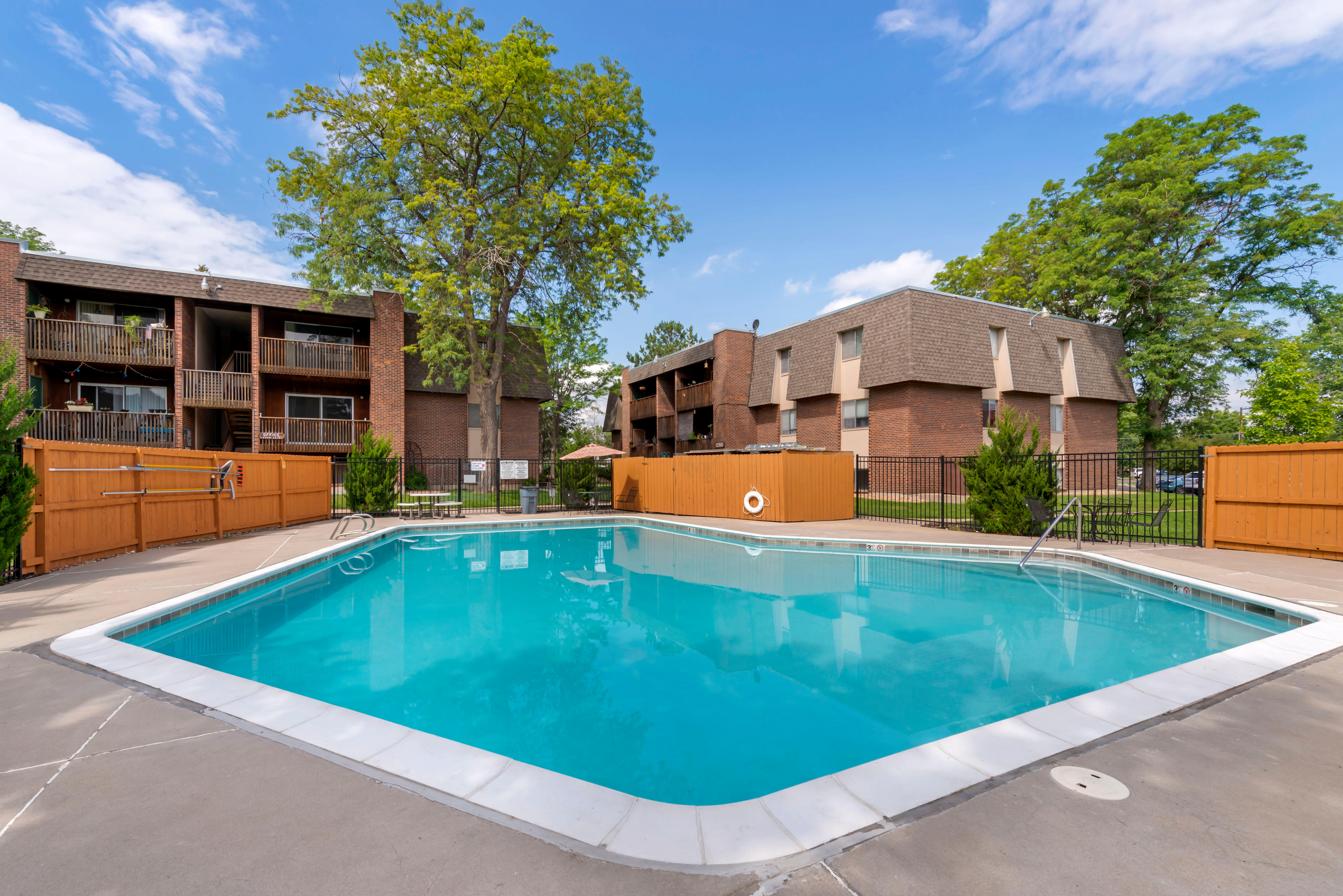 Community pool surrounded by a wooden fence with the brick and wood property exterior in background.