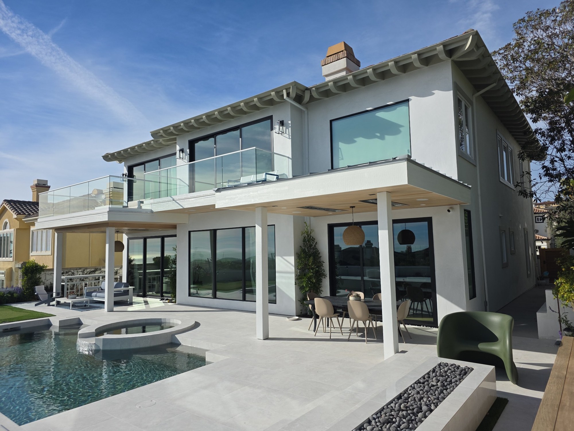 Completed exterior renovation with modern finishes, large windows, covered patio, and pool. 
