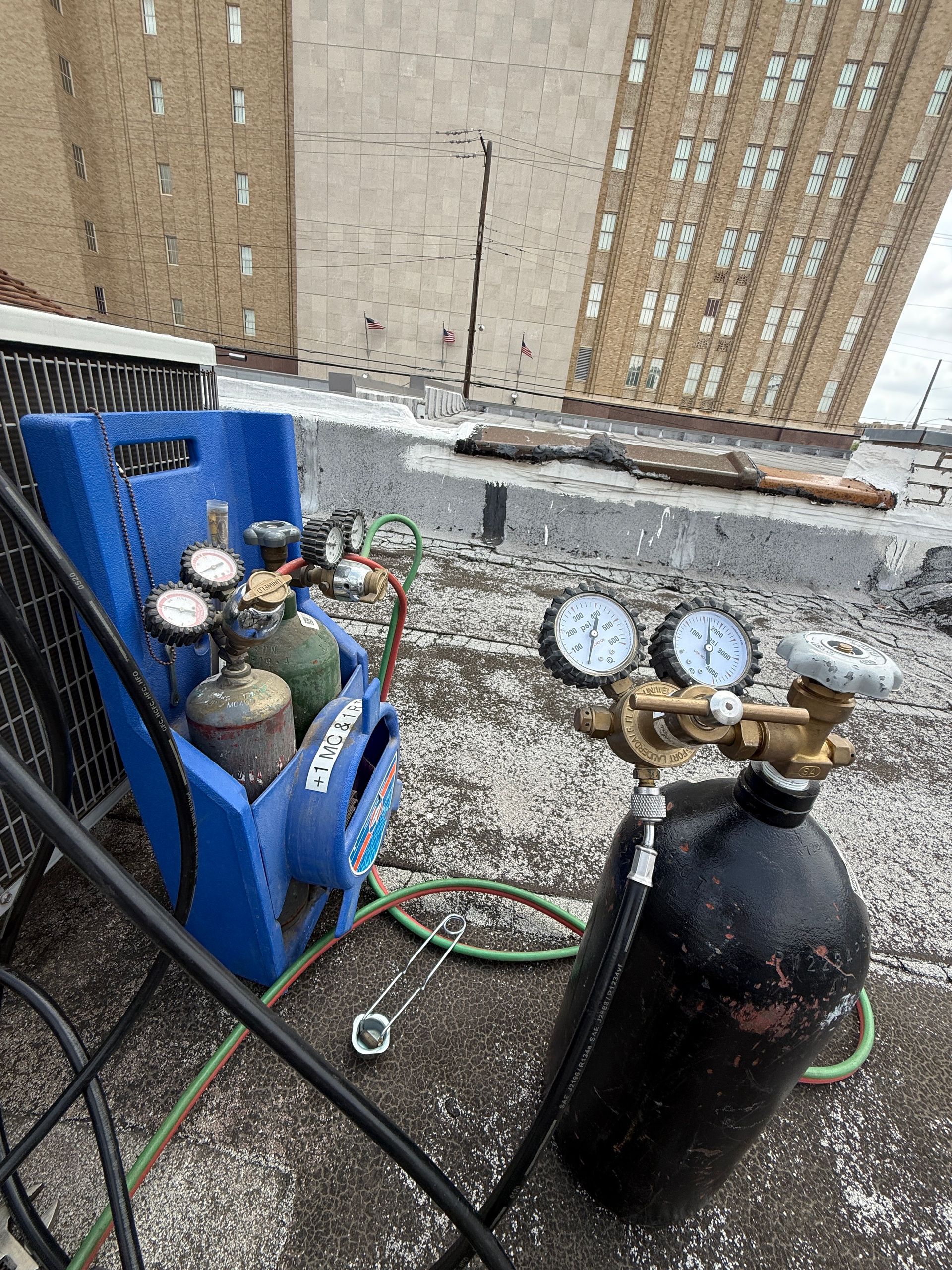 Refrigerant tanks and gauges on rooftop HVAC setup, used for charging or servicing cooling systems. Equipment positioned near commercial building, indicating professional maintenance, pressure control, and system diagnostics.