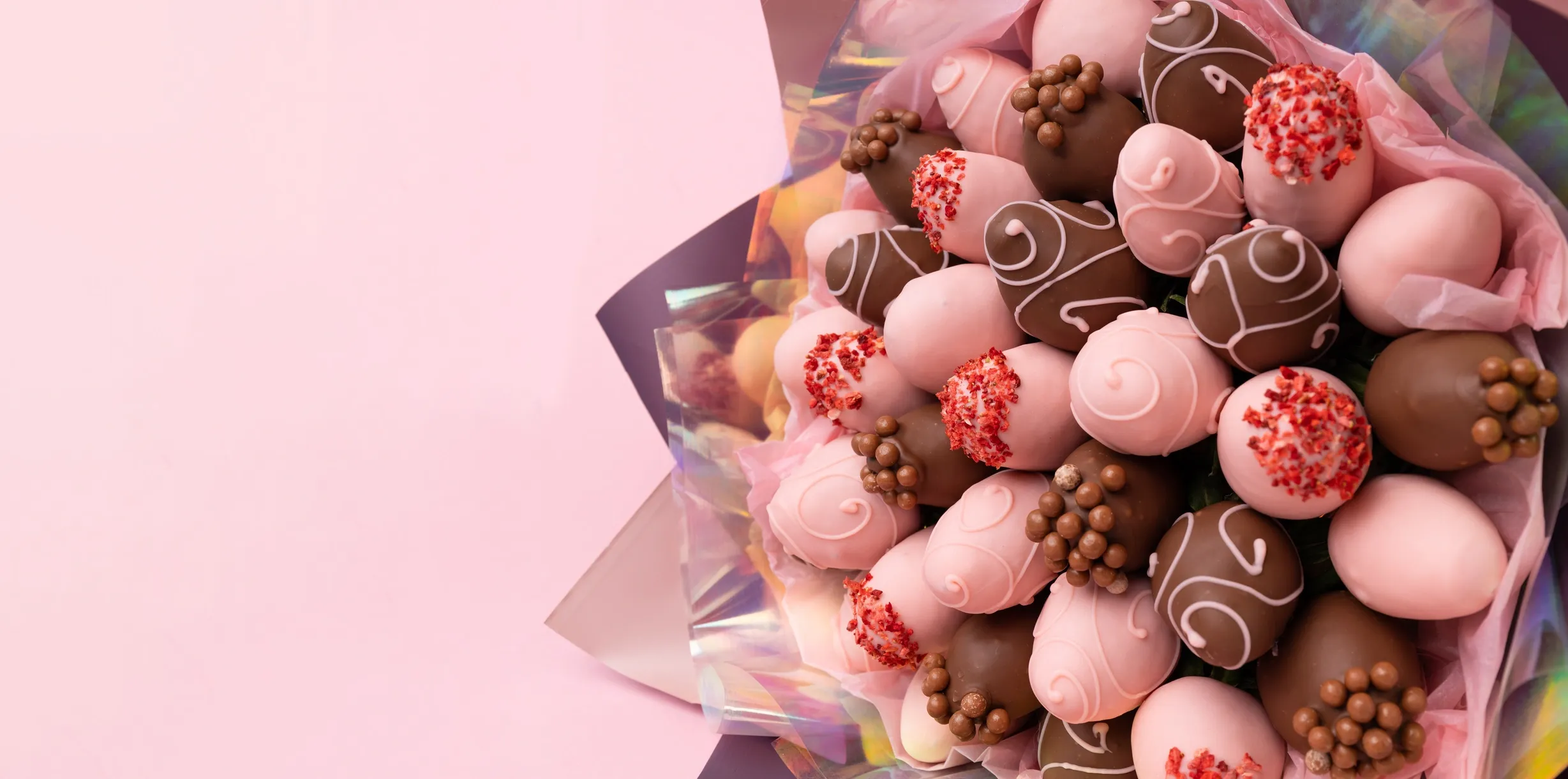 A bouquet of chocolate-covered strawberries arranged in a floral presentation, with a plain pink bac 