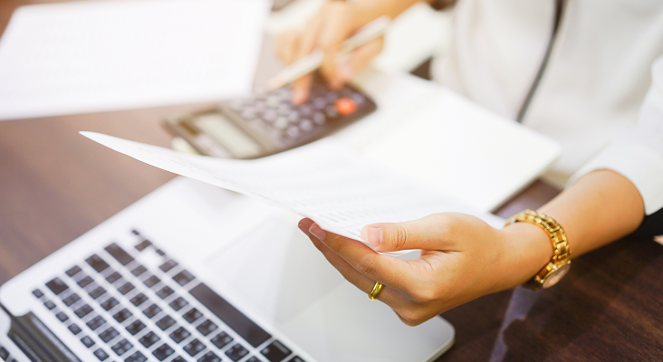 A person reviewing a document while typing on a calculator.