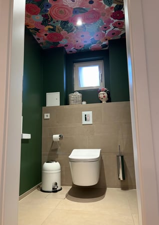 Aus einem funktionalen Gäste-WC ist ein Raum mit echtem Statement-Charakter entstanden. Die tiefgrünen Wände verleihen dem schmalen Raum Tiefe und Eleganz, während die florale Decke den Blick bewusst nach oben lenkt und für einen überraschenden Wow-...
