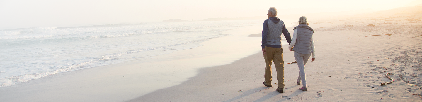 An elderly couple walking hand-in-hand along the beach.