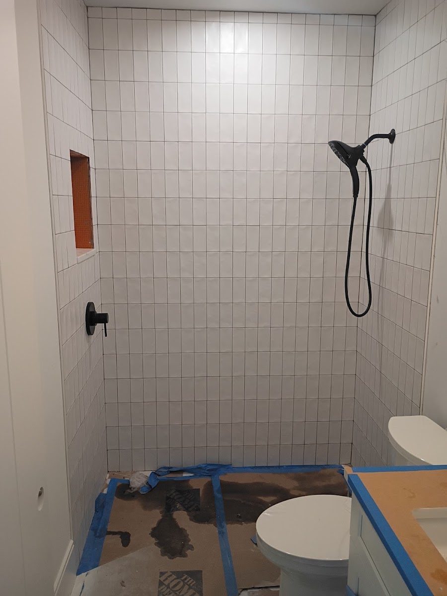 Bathroom shower installation with new wall tile, shower fixture, and plumbing connections being completed during renovation.