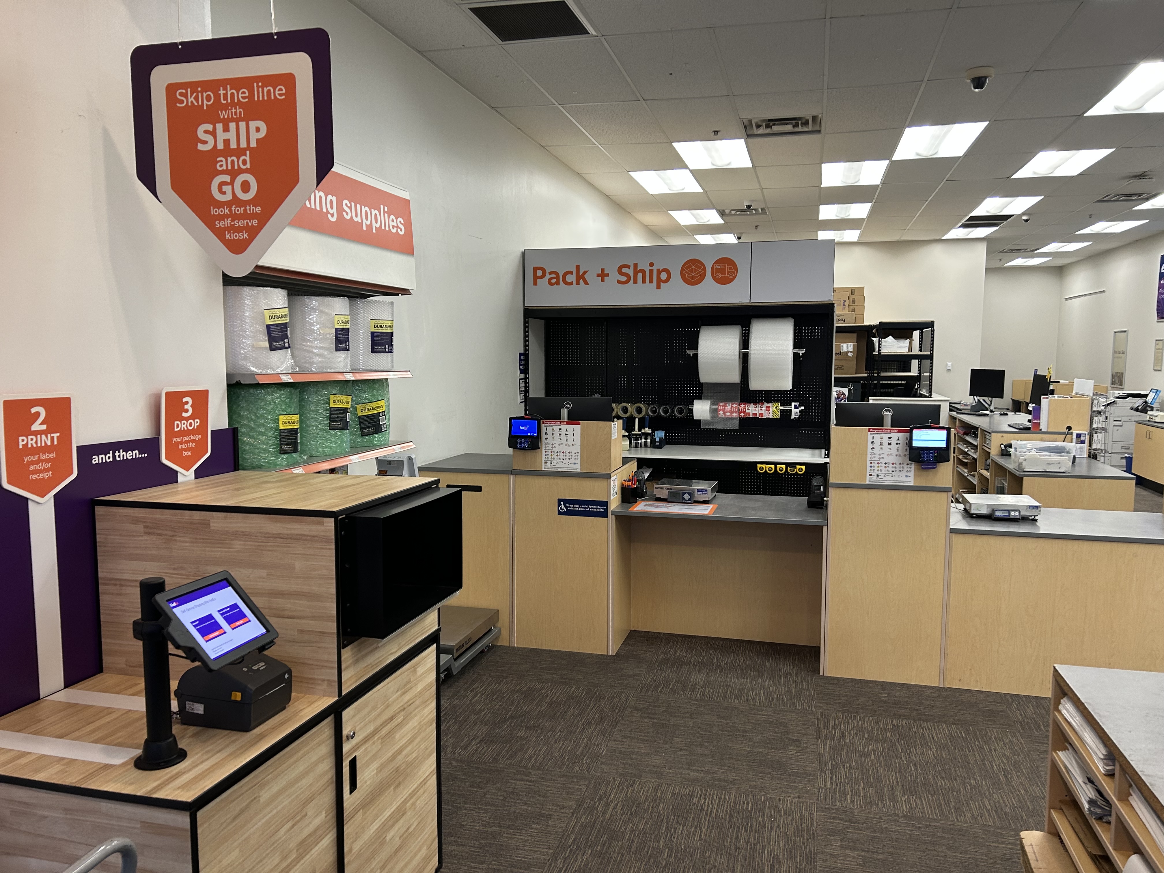 Pack and Ship Area with Ship and Go Kiosk &ndash; Pack and ship station with self-service Ship and Go kiosk, supplies, tape, and packaging tools at FedEx Office in Burleson Texas supporting shipping and returns.