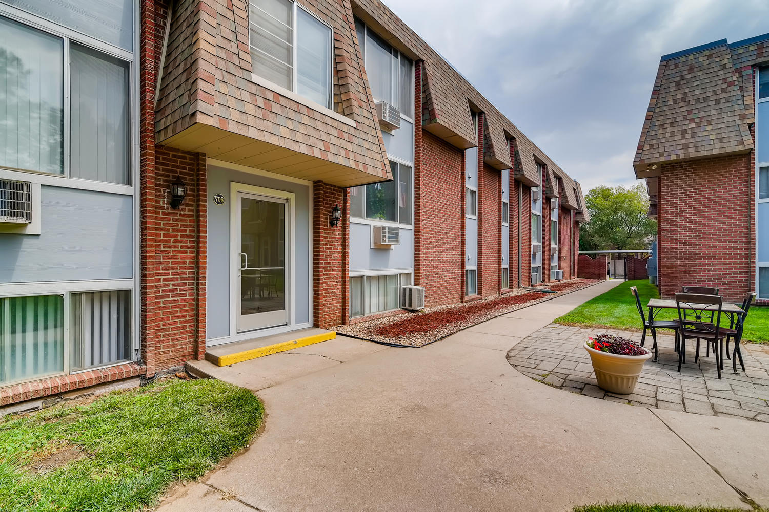 Brick and siding building exterior with sidewalk, picnic table and potted plant.