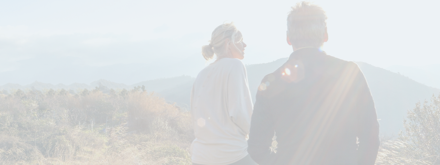 A man and woman sitting on a hill taking in the view of the mountains on a sunny day.
